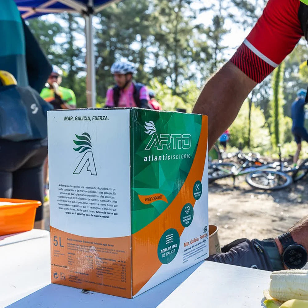 Artio sport isotonic drink box in orange flavor, 5L packaging at outdoor event, promoting hydration for athletes.
