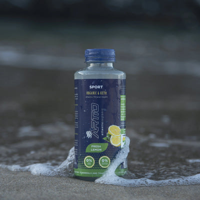 Artio sport isotonic drink in lemon flavor, sugar-free, vegan, and gluten-free, placed on sandy beach.