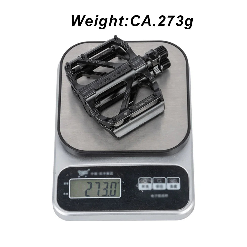Lightweight road bike pedal weighing 273g on a digital scale, showcasing its non-slip design and durable construction.