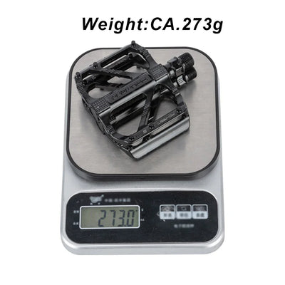 Lightweight road bike pedal weighing 273g on a digital scale, showcasing its non-slip design and durable construction.