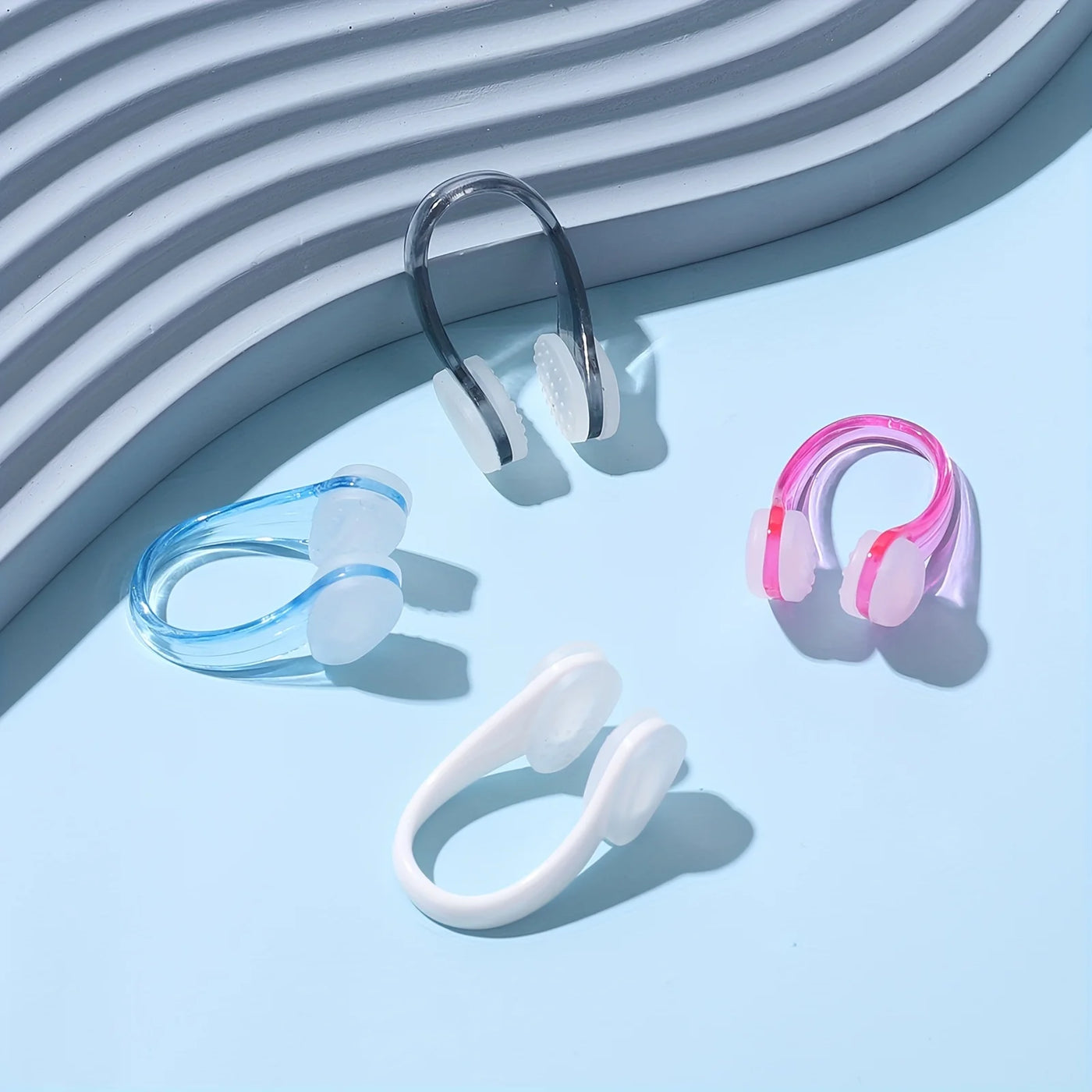 Four professional swimming nose clips in blue, clear, pink, and white on a light blue background, waterproof and non-slip design.