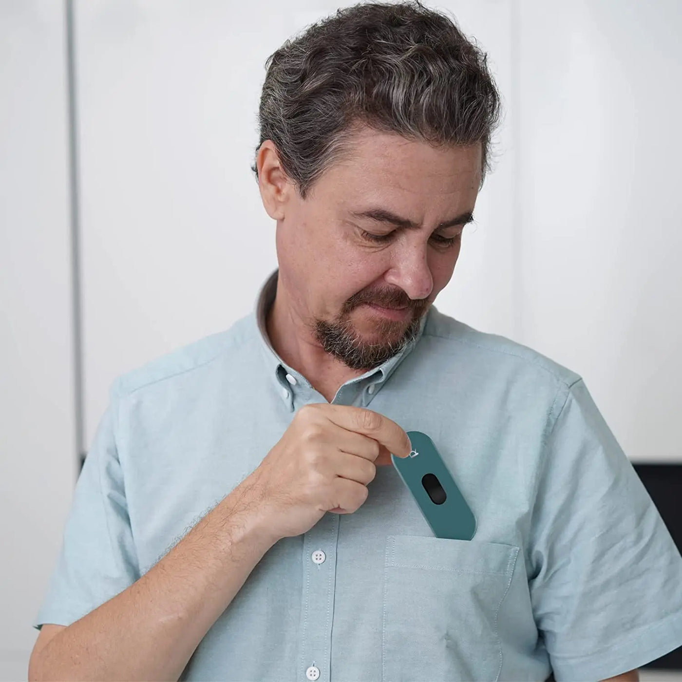 Man placing a Pocket ECG Monitor with OLED into his shirt pocket, showcasing its portable design and AI features.