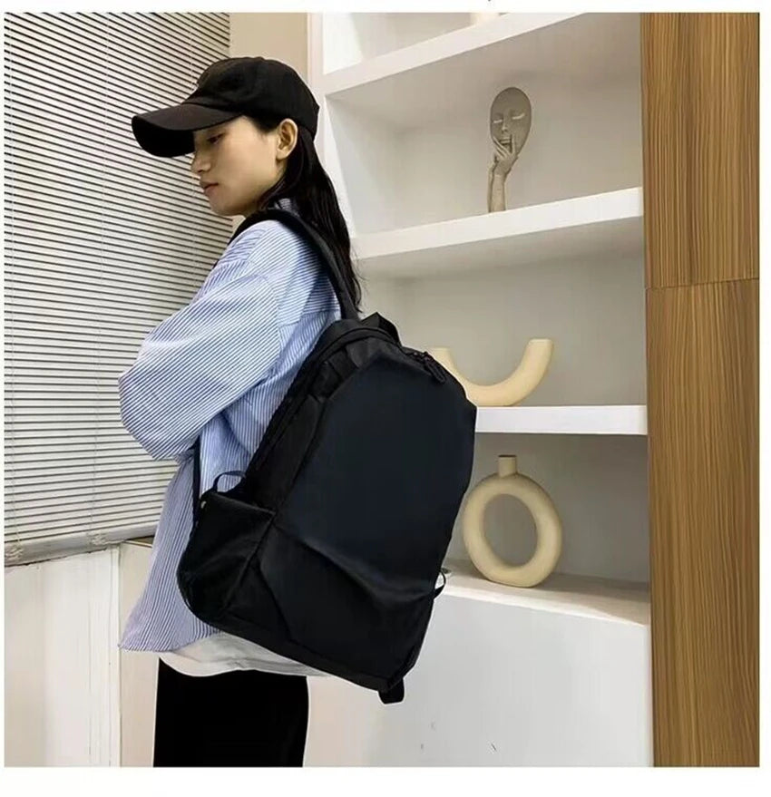 Side view of a woman wearing a black unisex backpack, showcasing its stylish design and practical use for students.