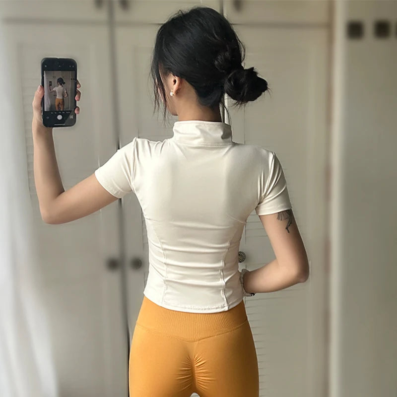 Back view of a woman wearing a cream short-sleeved slimming yoga top with a stand collar and stylish leggings.