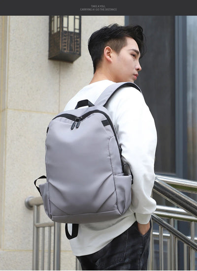 Gray unisex backpack worn by a young man, featuring soft handles and a sleek design, perfect for college or travel.