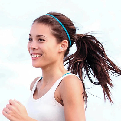 Woman jogging outdoors wearing a headband and Bluetooth wireless earbuds, smiling and enjoying active lifestyle.