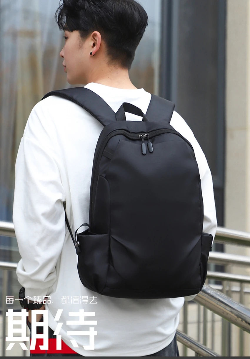 Black unisex backpack worn by a student on campus, ideal for college and everyday use.