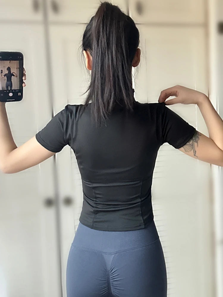 Back view of a woman wearing a women’s slimming black yoga top with short sleeves and stand collar.