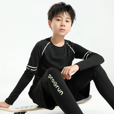 Young boy in black thermal compression sportswear, sitting on a skateboard, showcasing quick-dry features for active play.