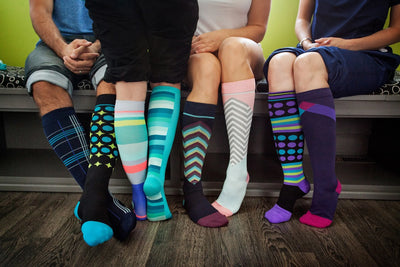 Group of people wearing colorful knee-high compression socks in various patterns and styles.