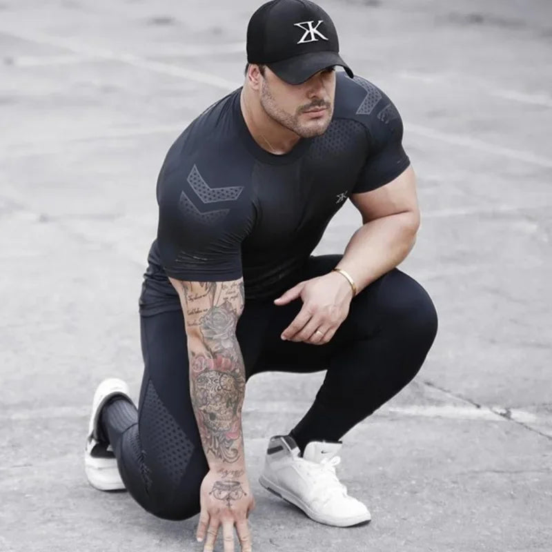 Man in fitness apparel kneeling, wearing a black training tee and leggings for bodybuilding and workouts.