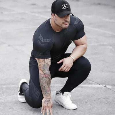 Man in fitness apparel kneeling, wearing a black training tee and leggings for bodybuilding and workouts.