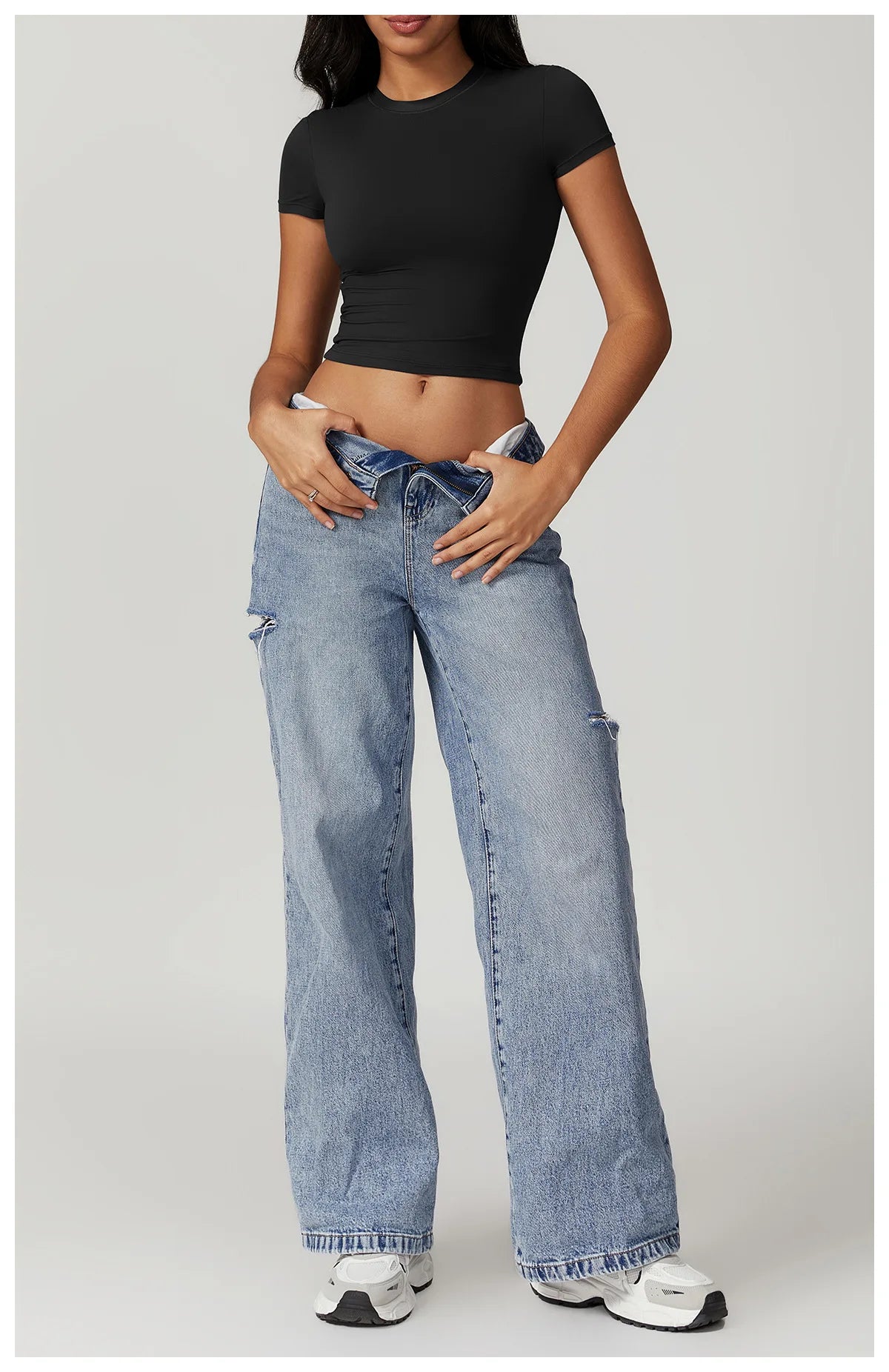 Model wearing a fitted black crop top with loose blue jeans and sneakers, showcasing a casual, stylish look.