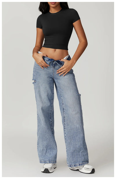 Model wearing a fitted black crop top with loose blue jeans and sneakers, showcasing a casual, stylish look.