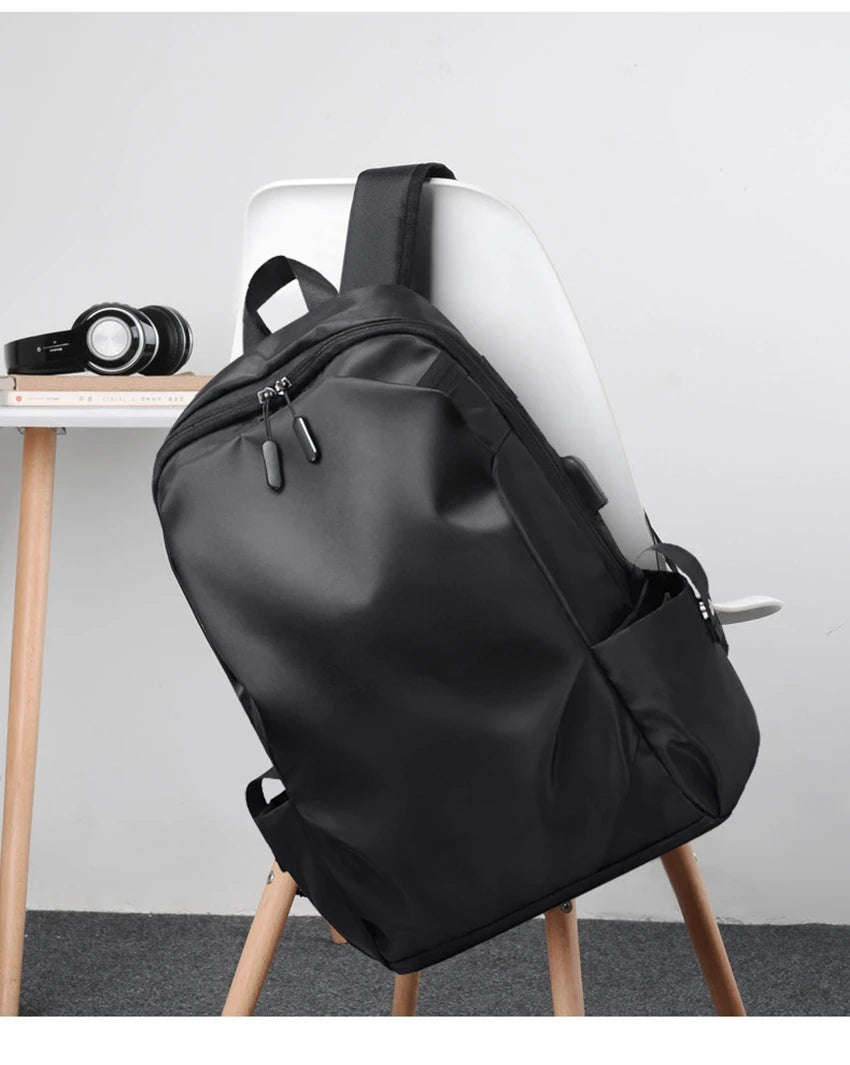 Sleek black unisex laptop backpack displayed on a chair, ideal for students with USB port and soft handle design.
