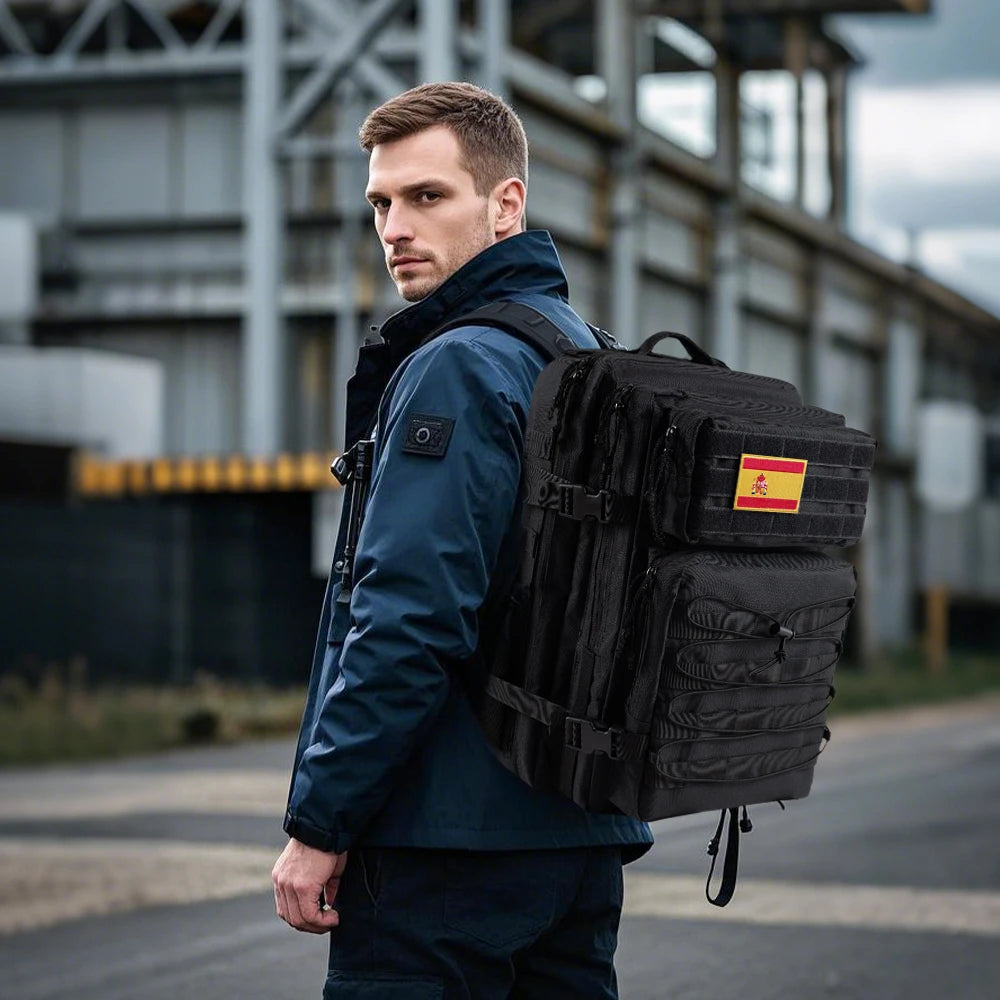 Man wearing a tactical backpack outdoors, showcasing a black multi-functional expansion rucksack with accessory patches.