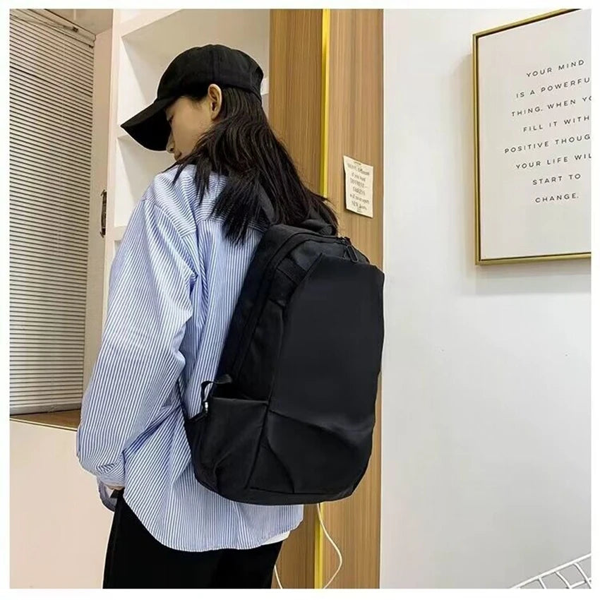 Unisex black backpack worn by a person in casual attire, showcasing a stylish design suitable for students.