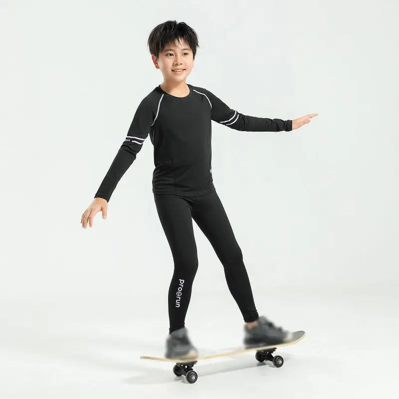 Boy wearing black thermal compression sportswear, balancing on a skateboard, showcasing athletic style and comfort.