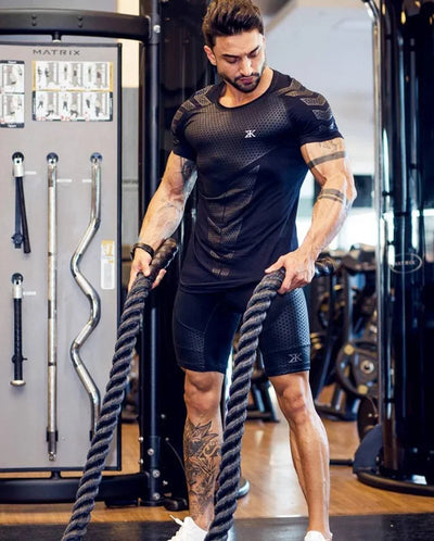 Man in black training shirt using battle ropes in gym, showcasing fitness and bodybuilding style.