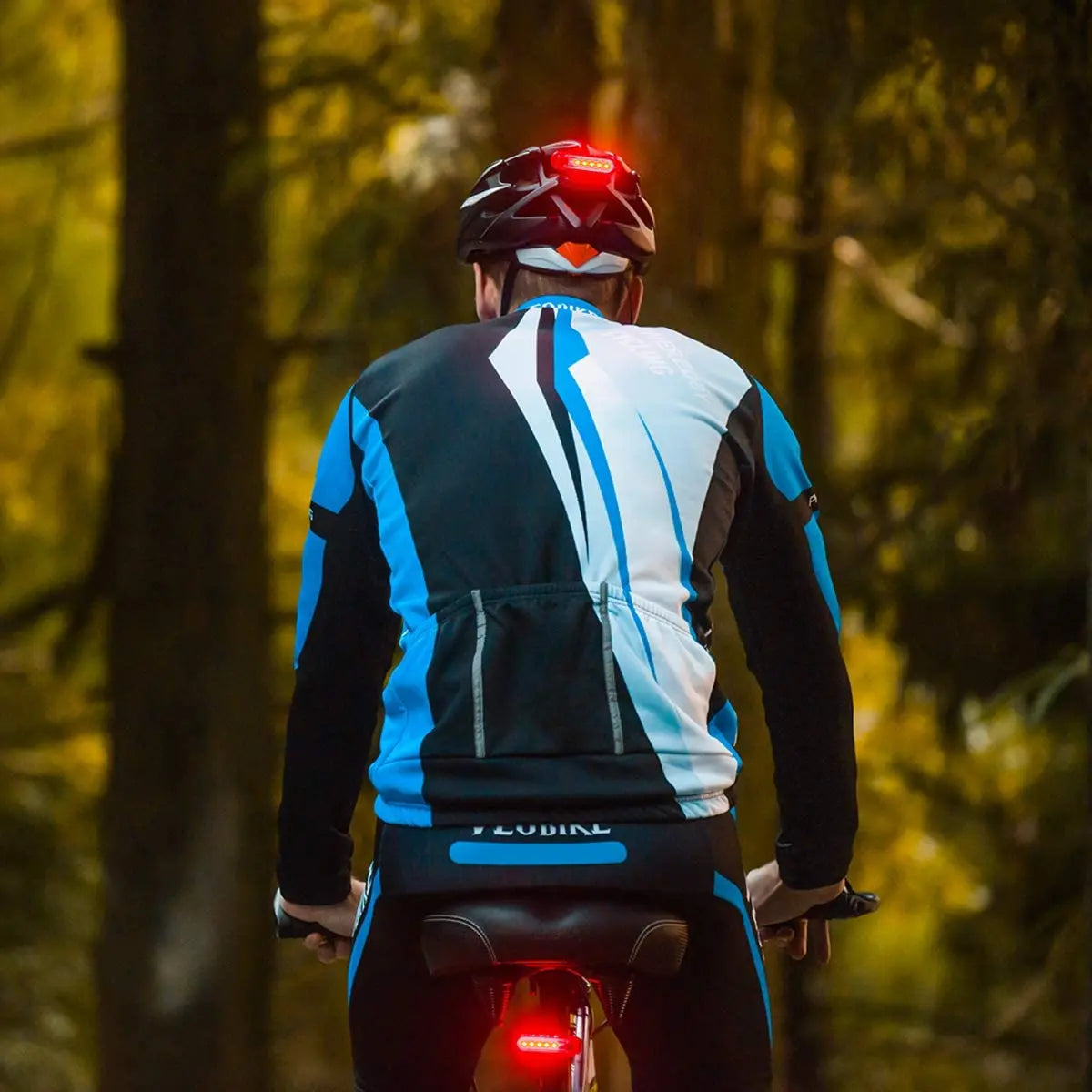 Cyclist riding a bike in the woods featuring a USB rechargeable ultra bright red tail light for safety.