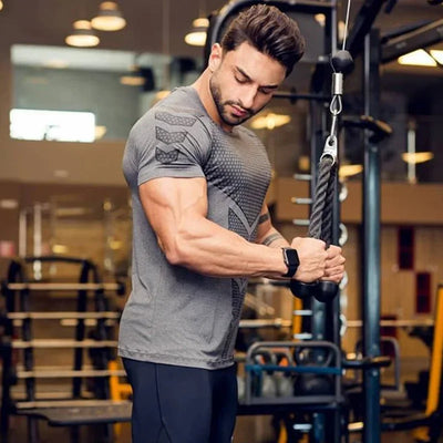 Man exercising in a grey 2024 men’s quick dry running sports T-shirt, showcasing a muscular build in a gym setting.