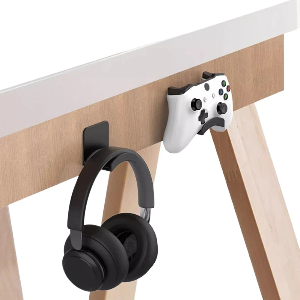Universal adhesive headset hanger holding black headphones under a desk alongside an Xbox controller.