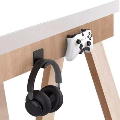 Universal adhesive headset hanger holding black headphones under a desk alongside an Xbox controller.