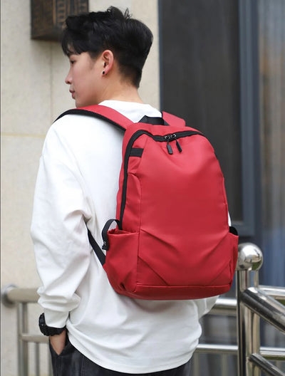 Unisex red nylon backpack on a young man, perfect for college students, featuring a soft handle and zipper closure.