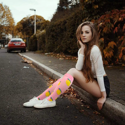Young woman sitting on street wearing colorful knee-high socks with pineapple print and casual outfit.
