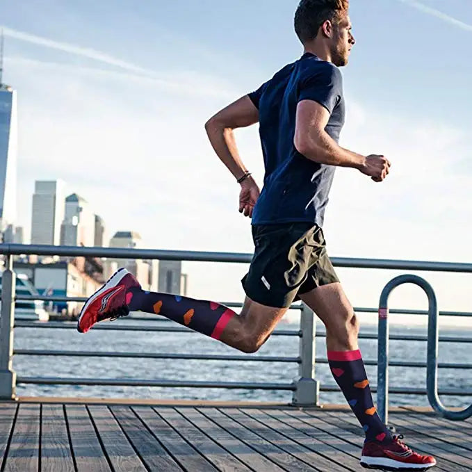 Man running on a pier, wearing colorful knee-high compression socks and athletic shoes, with city skyline in background.