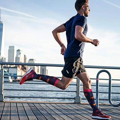 Man running on a pier, wearing colorful knee-high compression socks and athletic shoes, with city skyline in background.