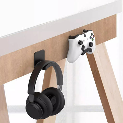 Black headphone and white gaming controller mounted on a wall desk with adhesive hooks for easy organization.