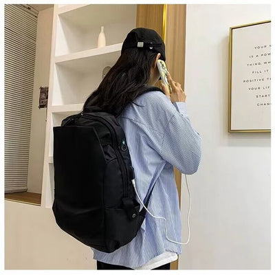 Unisex black backpack worn by a student talking on the phone, featuring USB port and soft straps.