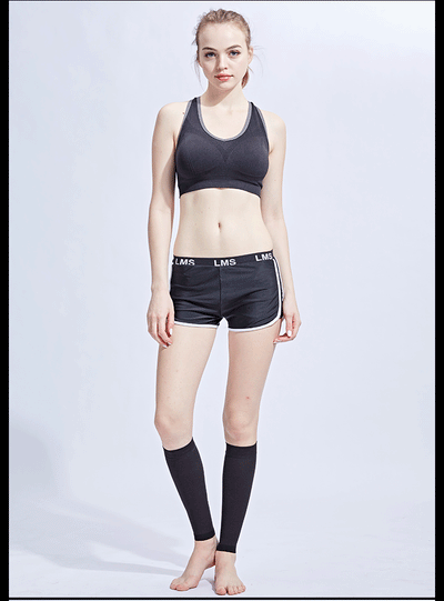 Model wearing a black sports bra, shorts, and compression calf sleeves, showcasing athletic wear for fitness or sports activities.