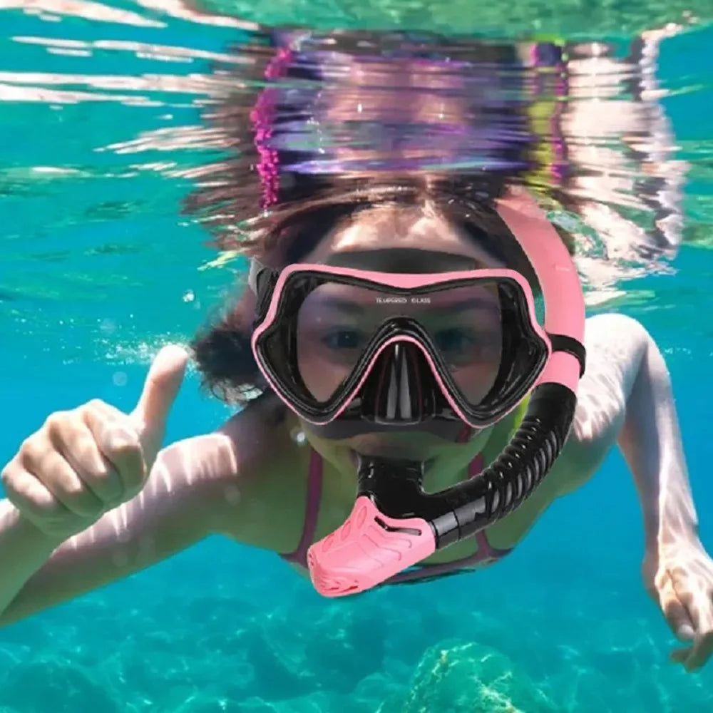 Adult wearing a pink and black scuba diving mask and snorkel, giving a thumbs up underwater, showcasing snorkeling gear.