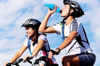 Active adults cycling outdoors, enjoying Benedetto Upgrade Blue isotonic sports drink for hydration.